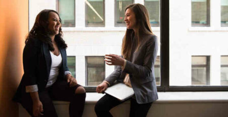 Two women sitting by the window laughing.