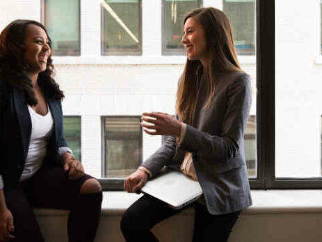 Two women sitting by the window laughing.