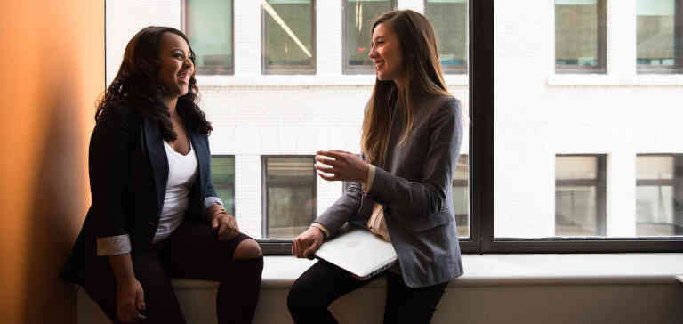 Two women sitting by the window laughing.