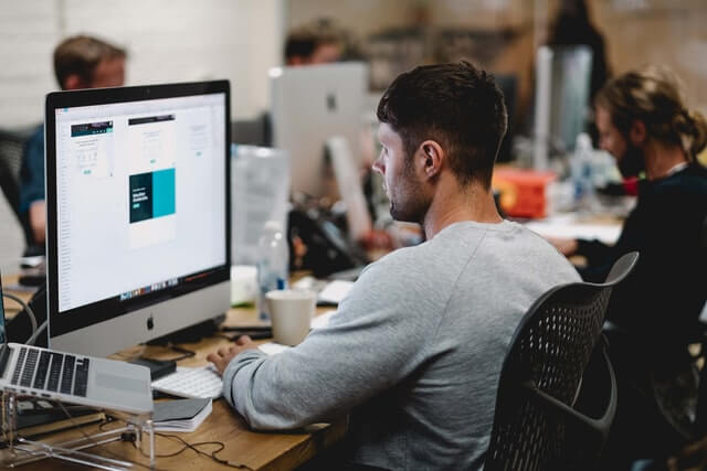 A young man working in an office on a Macbook.