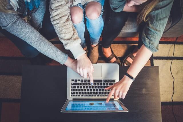 Three women point to a silver laptop screen.