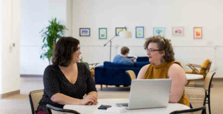 Two women sitting at a desk in an office.