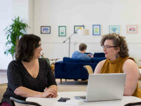 Two women sitting at a desk in an office.