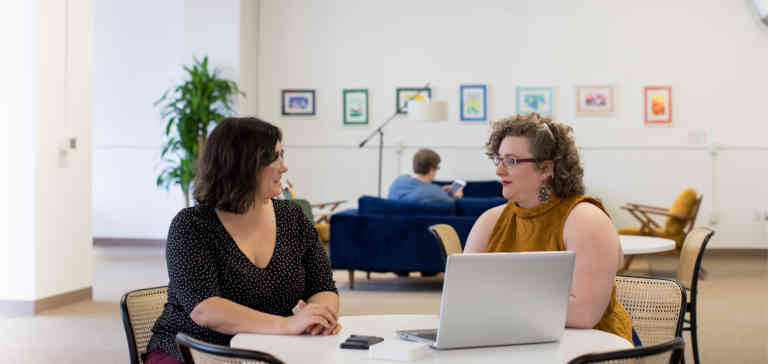 Two women sitting at a desk in an office.