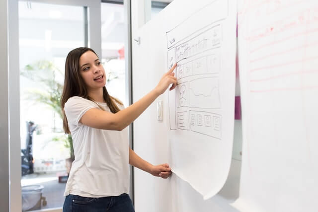 Woman standing pointing to a piece of paper.