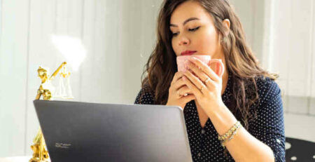 A woman drinking coffee and looking at a computer.