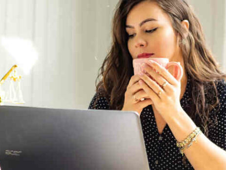 A woman drinking coffee and looking at a computer.