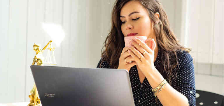 A woman drinking coffee and looking at a computer.