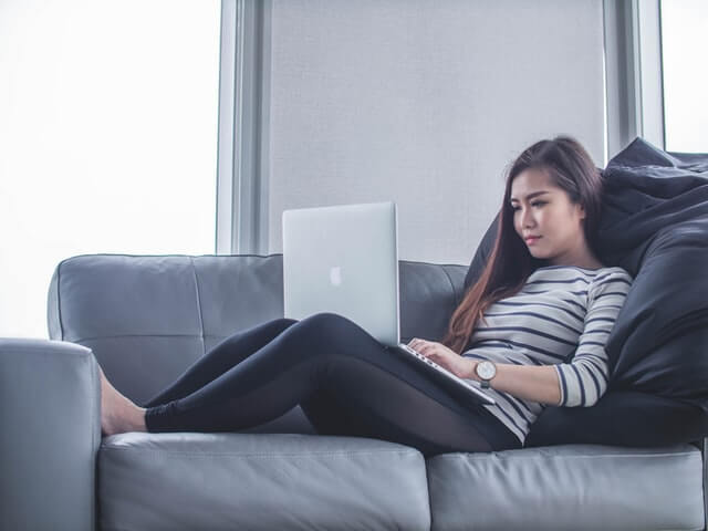 Woman using a laptop sitting on the couch.