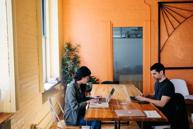 A man and woman working together at a wooden desk.