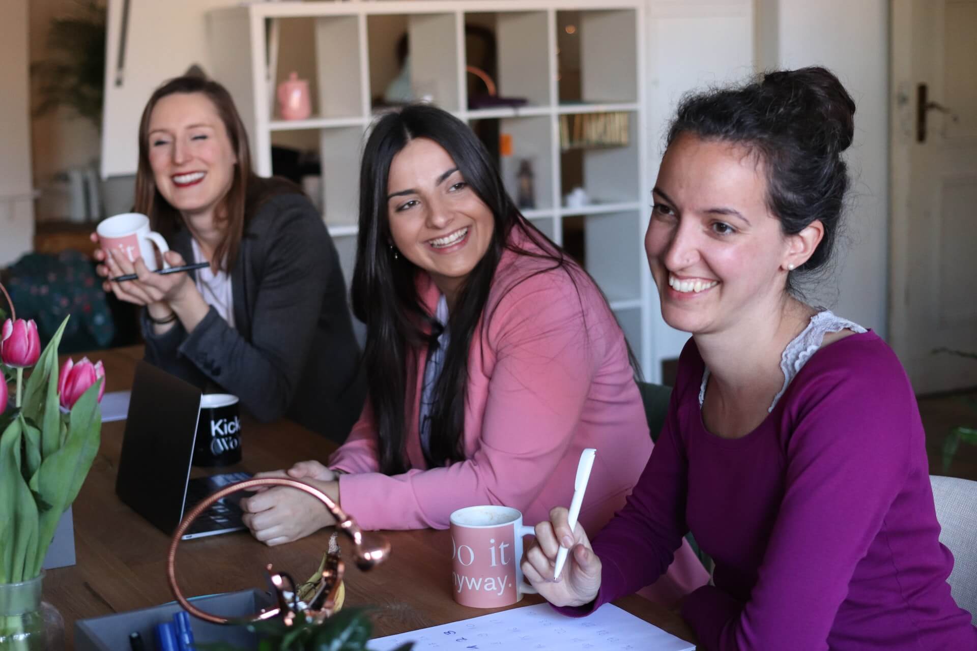 Three women having coffee at a table and smiling.