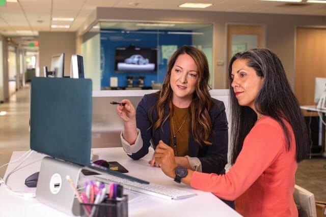 Two businesswomen talking near a computer.