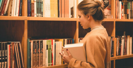 A woman chooses a book from a bookshelf.