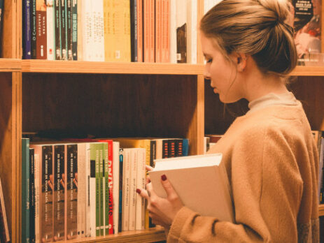 A woman chooses a book from a bookshelf.