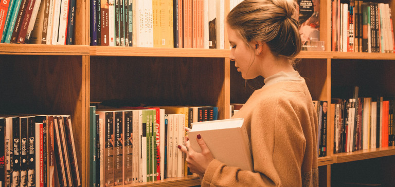 A woman chooses a book from a bookshelf.