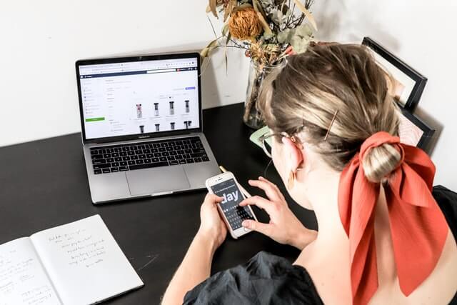 A woman uses her smartphone near a laptop.