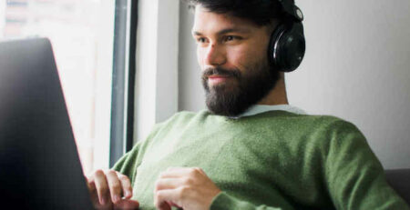 A man wearing a green shirt and headphones works on a laptop.