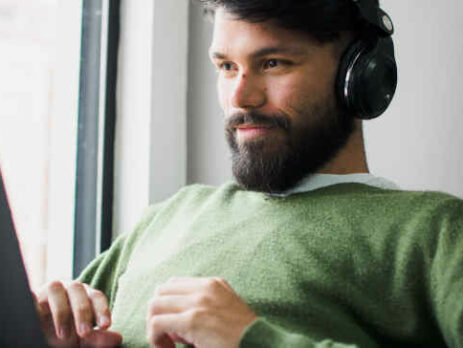 A man wearing a green shirt and headphones works on a laptop.