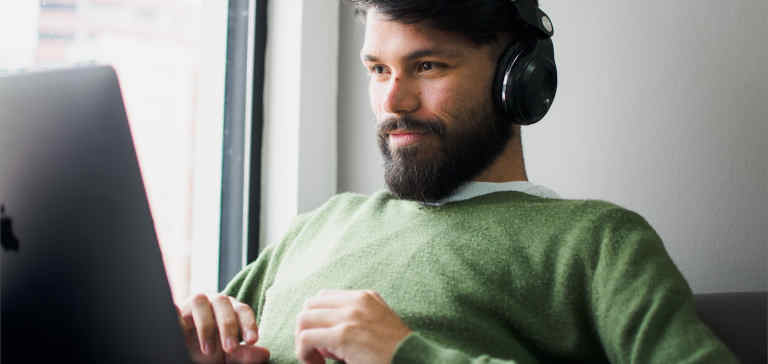 A man wearing a green shirt and headphones works on a laptop.