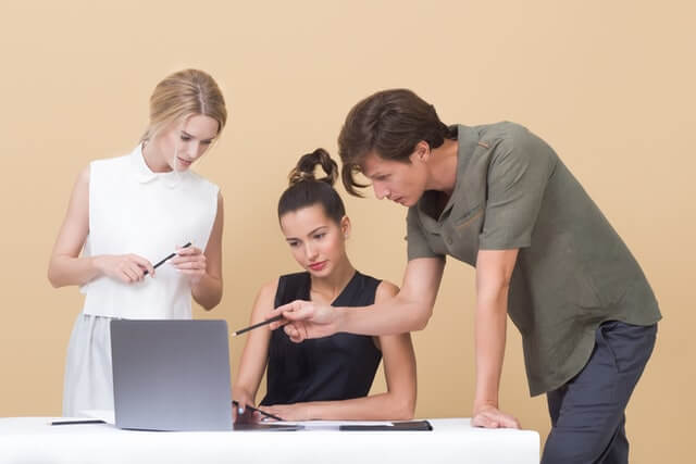 A man and two women talking near a laptop.