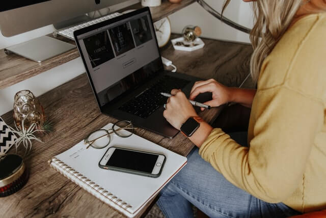 A woman in a yellow shirt works on a laptop.