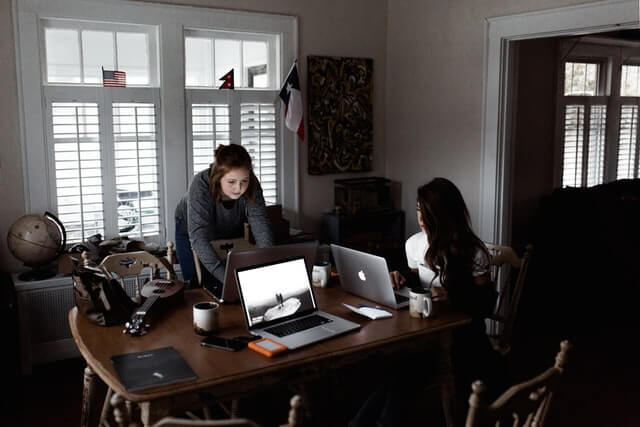 Two women working on laptops on a brown table.