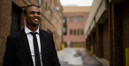 A smiling man in a business suit stands in the street.