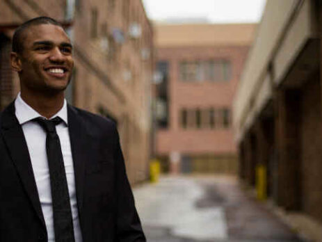 A smiling man in a business suit stands in the street.