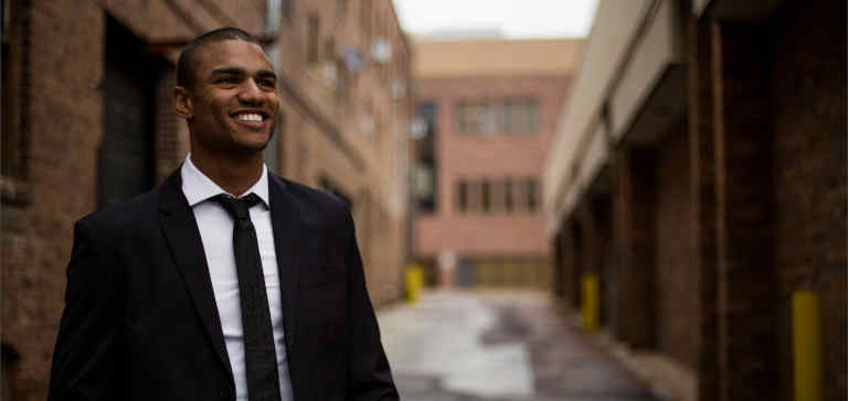 A smiling man in a business suit stands in the street.