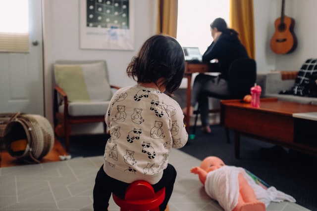 A child plays behind a man working on a computer.