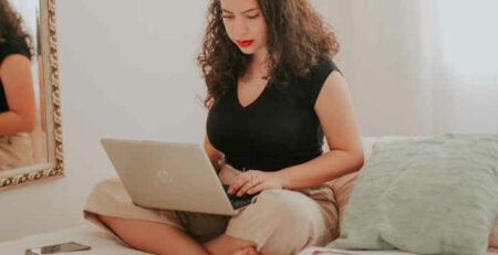 A woman in a black shirt works on a laptop.