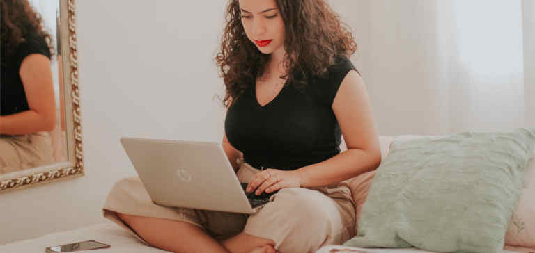 A woman in a black shirt works on a laptop.