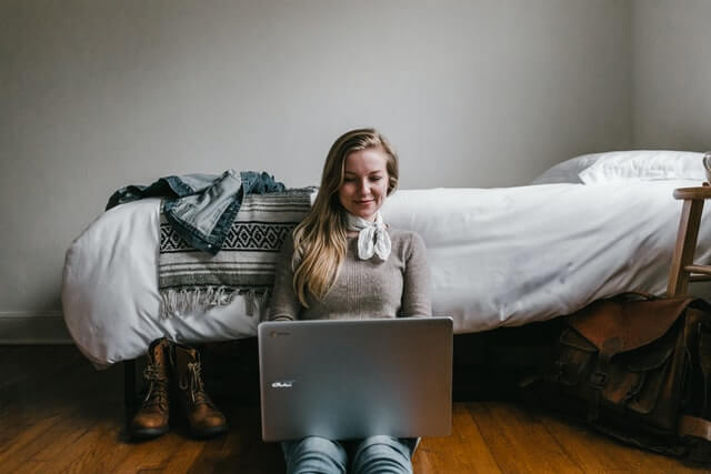 A woman with a white scarf works on a laptop in a bedroom.