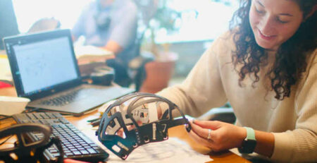A woman in a white long-sleeved shirt holding a prototype.