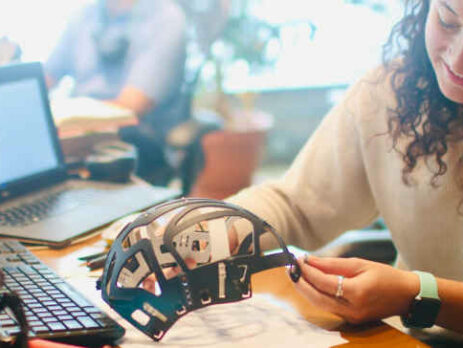 A woman in a white long-sleeved shirt holding a prototype.