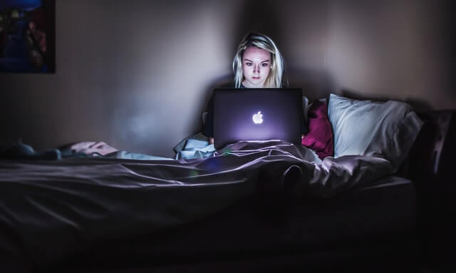A woman works on a laptop while sitting in a bed.