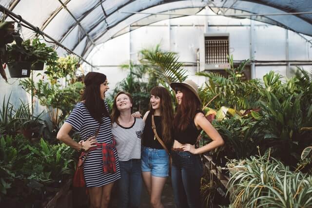 Four women laugh inside of a greenhouse.