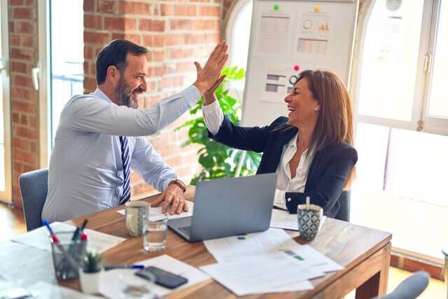 A man and a woman high five each other during a work meeting.