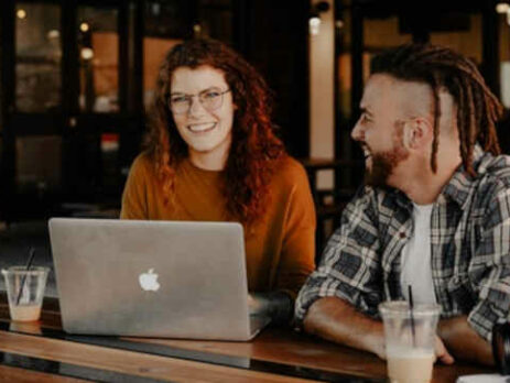 A man and a woman sit at a table with a laptop and a camera.