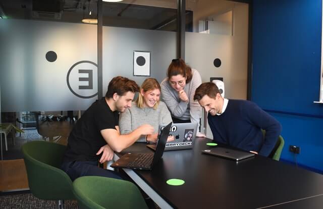 Two men and two women look at a computer during a work meeting.