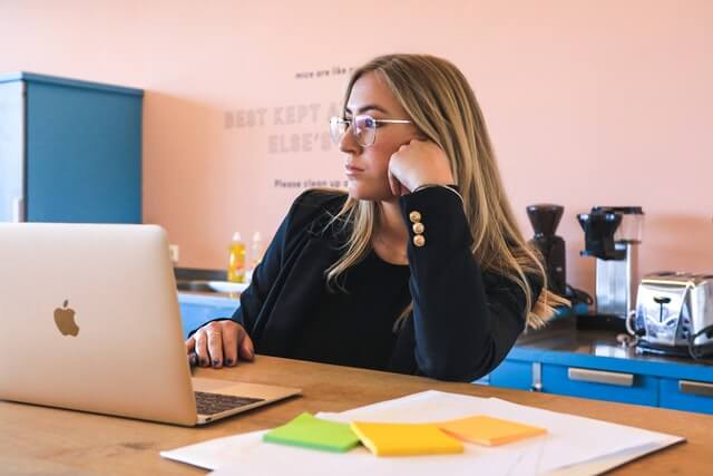 A woman wearing a black shirt and eyeglasses works on a laptop computer.