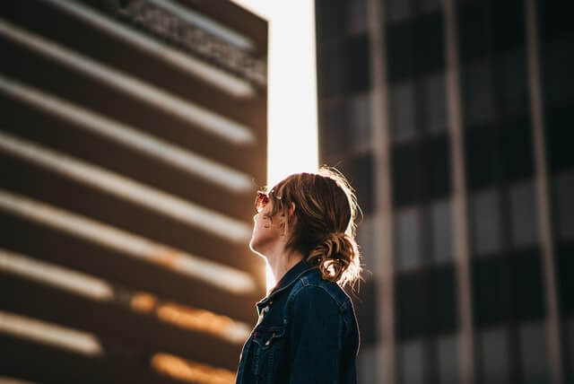 A woman in a jean jacket looks up at a tall building.