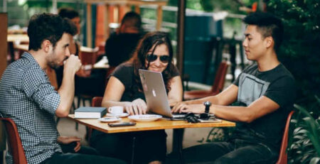 Two men and a woman sit at a coffee shop with a laptop.