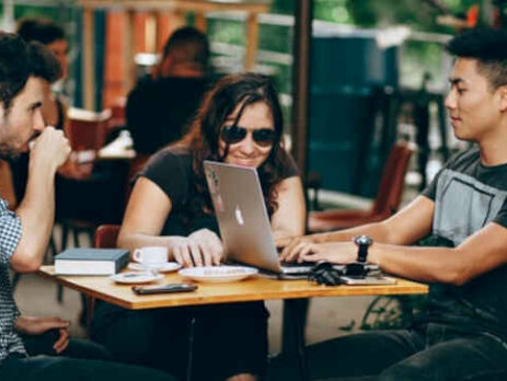 Two men and a woman sit at a coffee shop with a laptop.