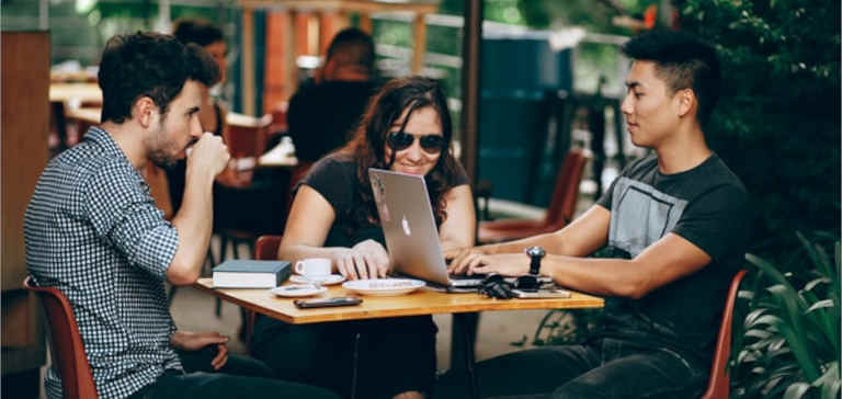 Two men and a woman sit at a coffee shop with a laptop.