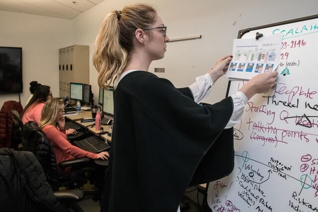 A woman wearing a black shirt posts a graph on a whiteboard.