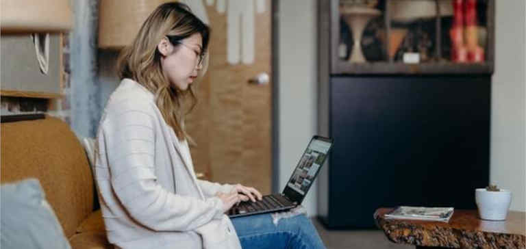 A woman wearing a white sweater works on a laptop at home.