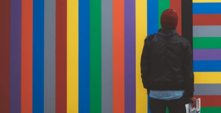 A man in a red beanie looks up at a colorful wall.