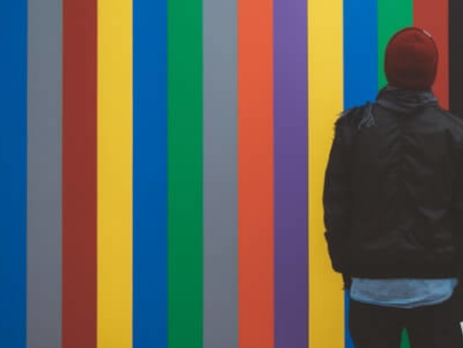 A man in a red beanie looks up at a colorful wall.
