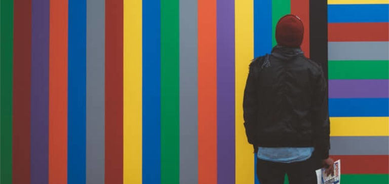 A man in a red beanie looks up at a colorful wall.